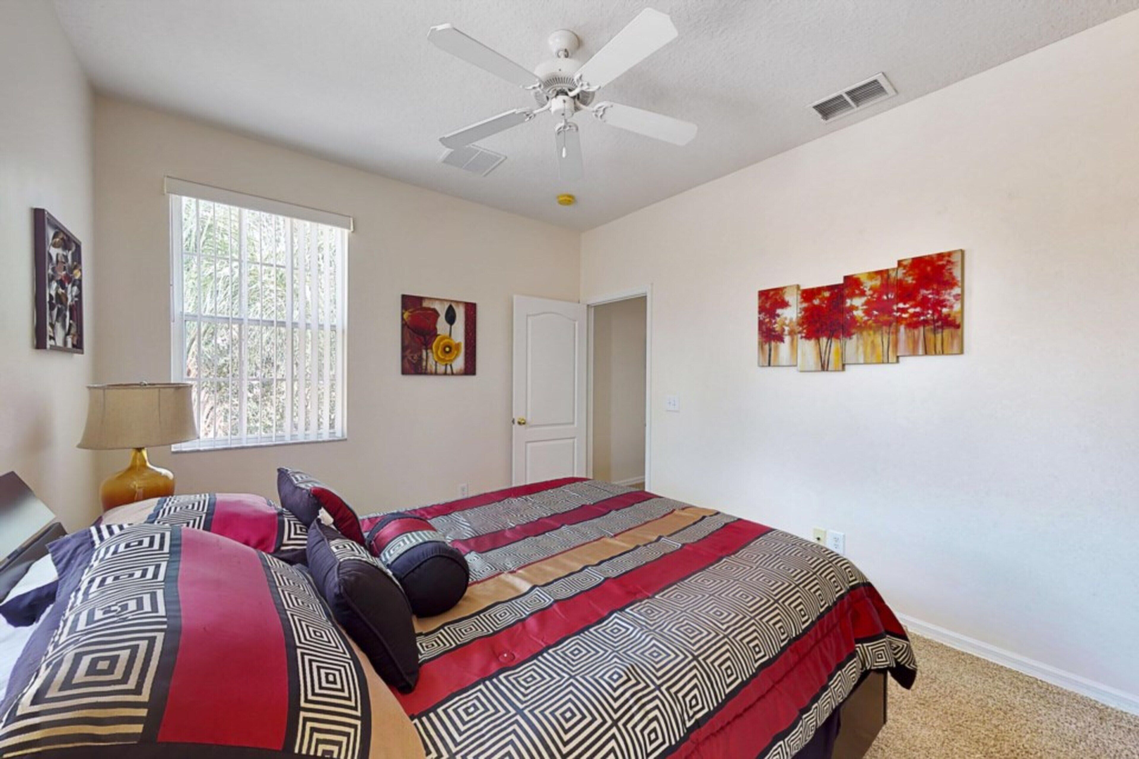 A bedroom with a bed, a ceiling fan, a window, and artwork on the walls.