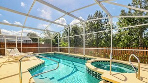 Une piscine intérieure protégée par une paroi de verre, deux chaises longues et une clôture en bois en arrière-plan.
