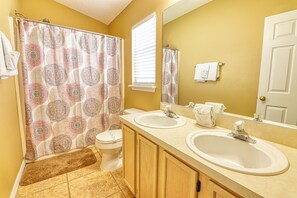 A bathroom with two sinks, a toilet, a shower curtain with a circular pattern, and a mirror above the sinks.