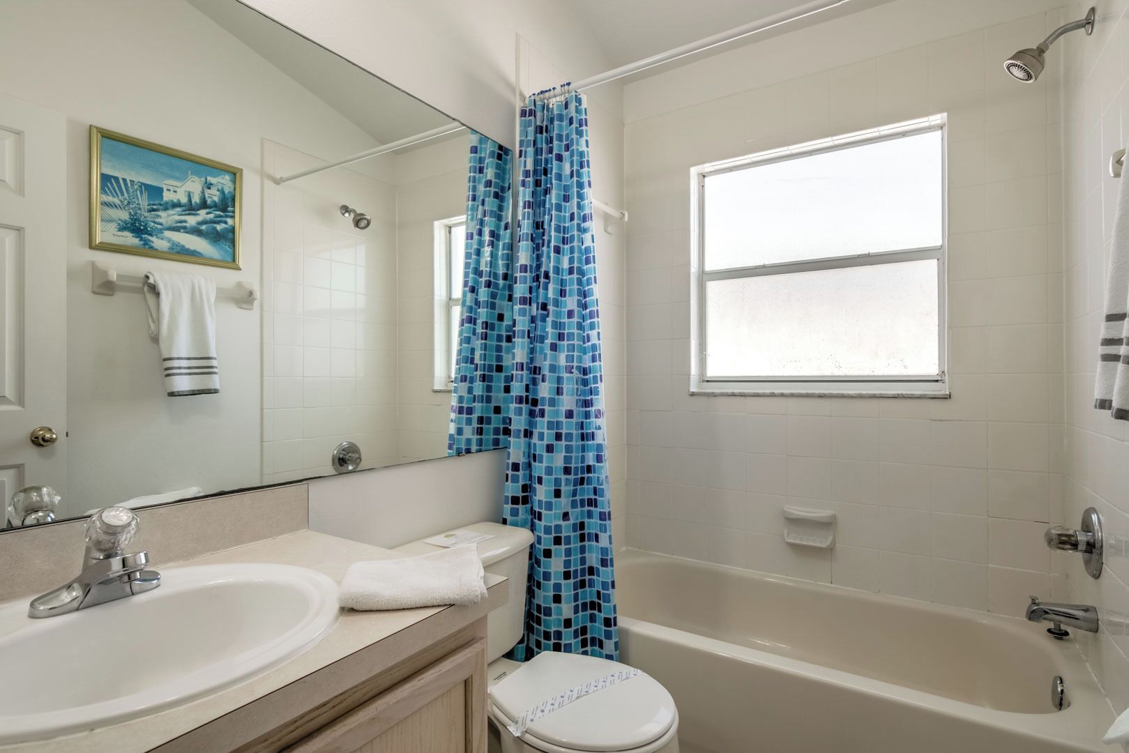 A bathroom with a sink, toilet, and bathtub. There is a window above the bathtub and a shower curtain with a blue pattern.