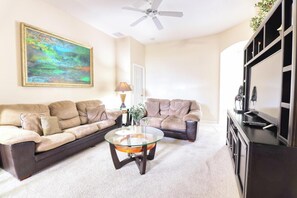 A living room with a beige sofa, a glass coffee table, a TV, and a painting on the wall.