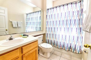A bathroom with a white sink, wooden cabinets, a toilet, and a shower curtain with a checkered pattern.