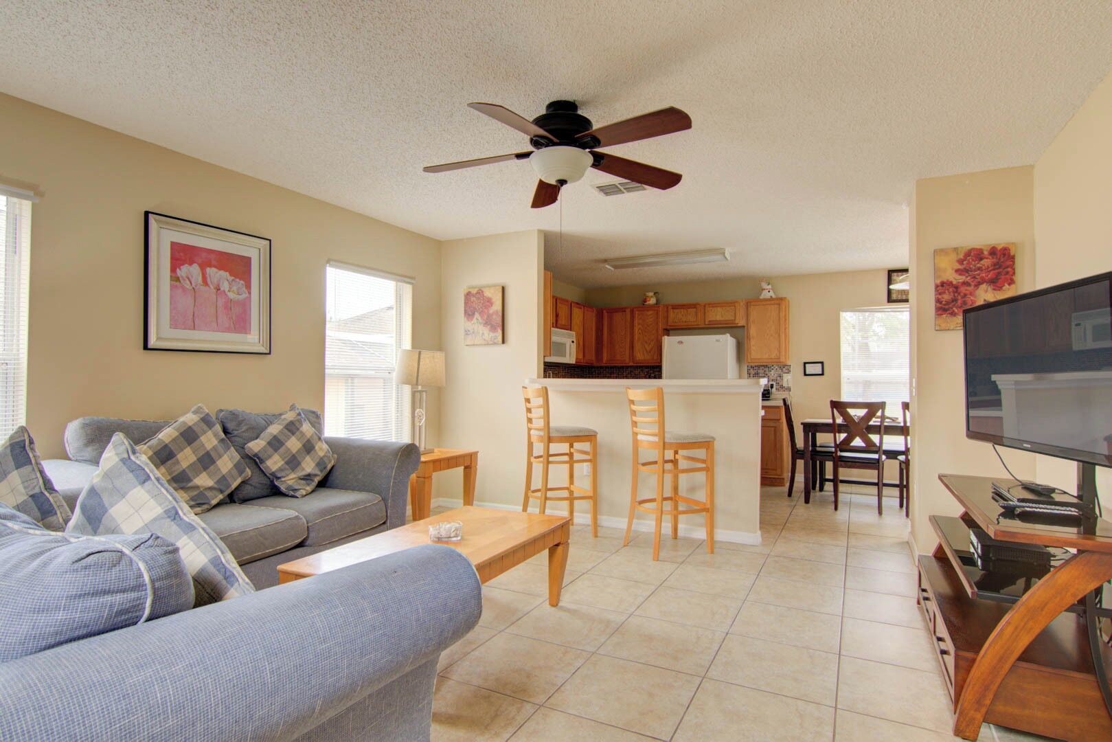 A living room with a sofa, coffee table, and TV stand. There is a kitchen area with a refrigerator, microwave, and dining table.
