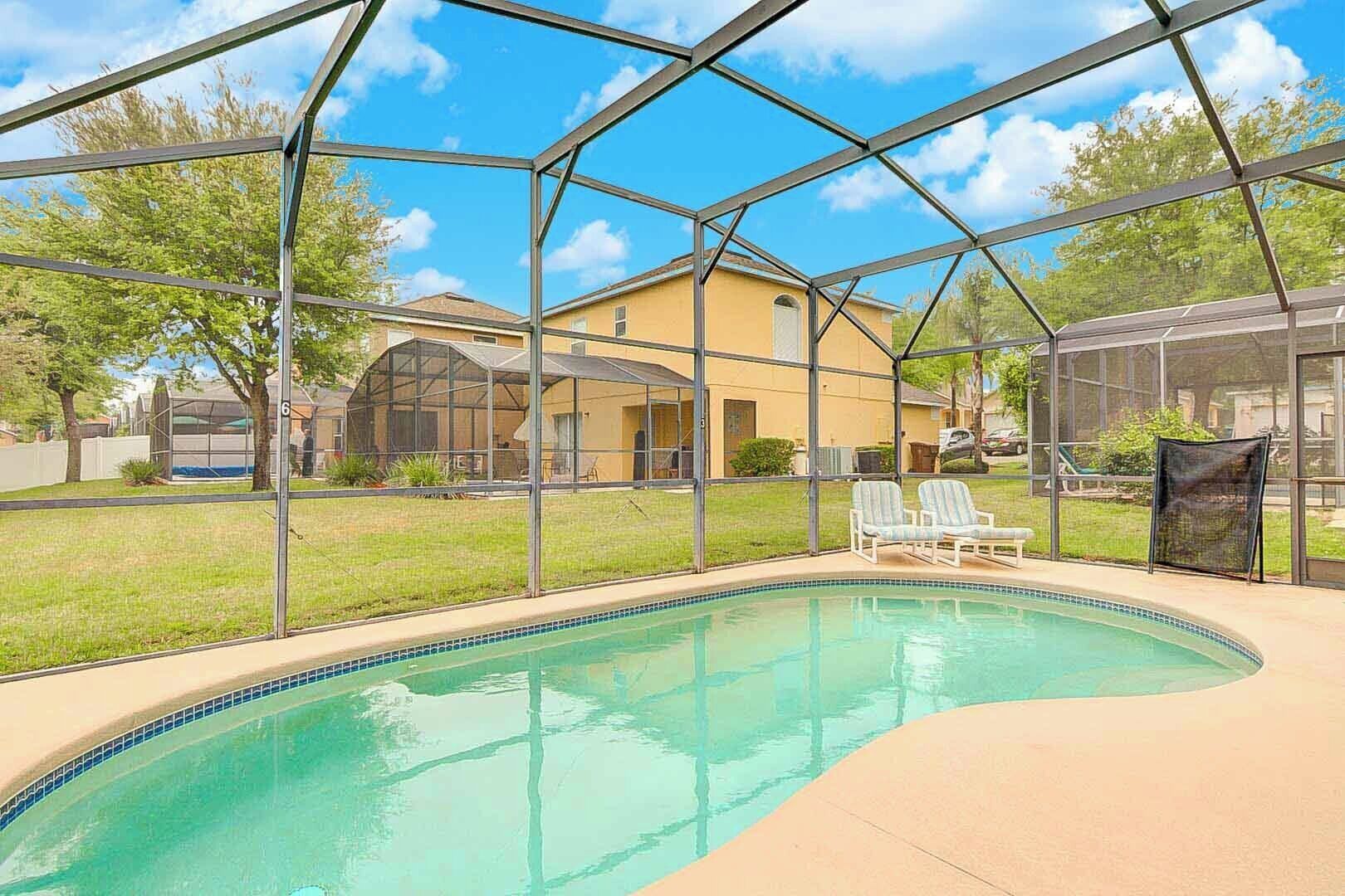 Ein Schwimmbad mit Glasüberdachung, umgeben von einer Rasenfläche und einem Haus.