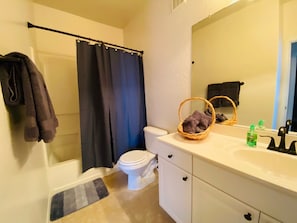 Une salle de bain avec un rideau de douche, des toilettes, un lavabo avec un miroir et un panier rempli de serviettes.