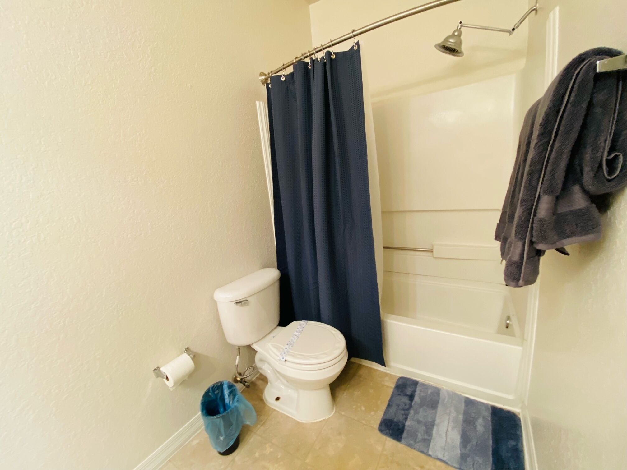 A bathroom with a toilet, a shower curtain, a towel rack, and a trash bin.