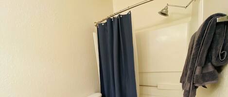 A bathroom with a toilet, a shower curtain, a towel rack, and a trash bin.