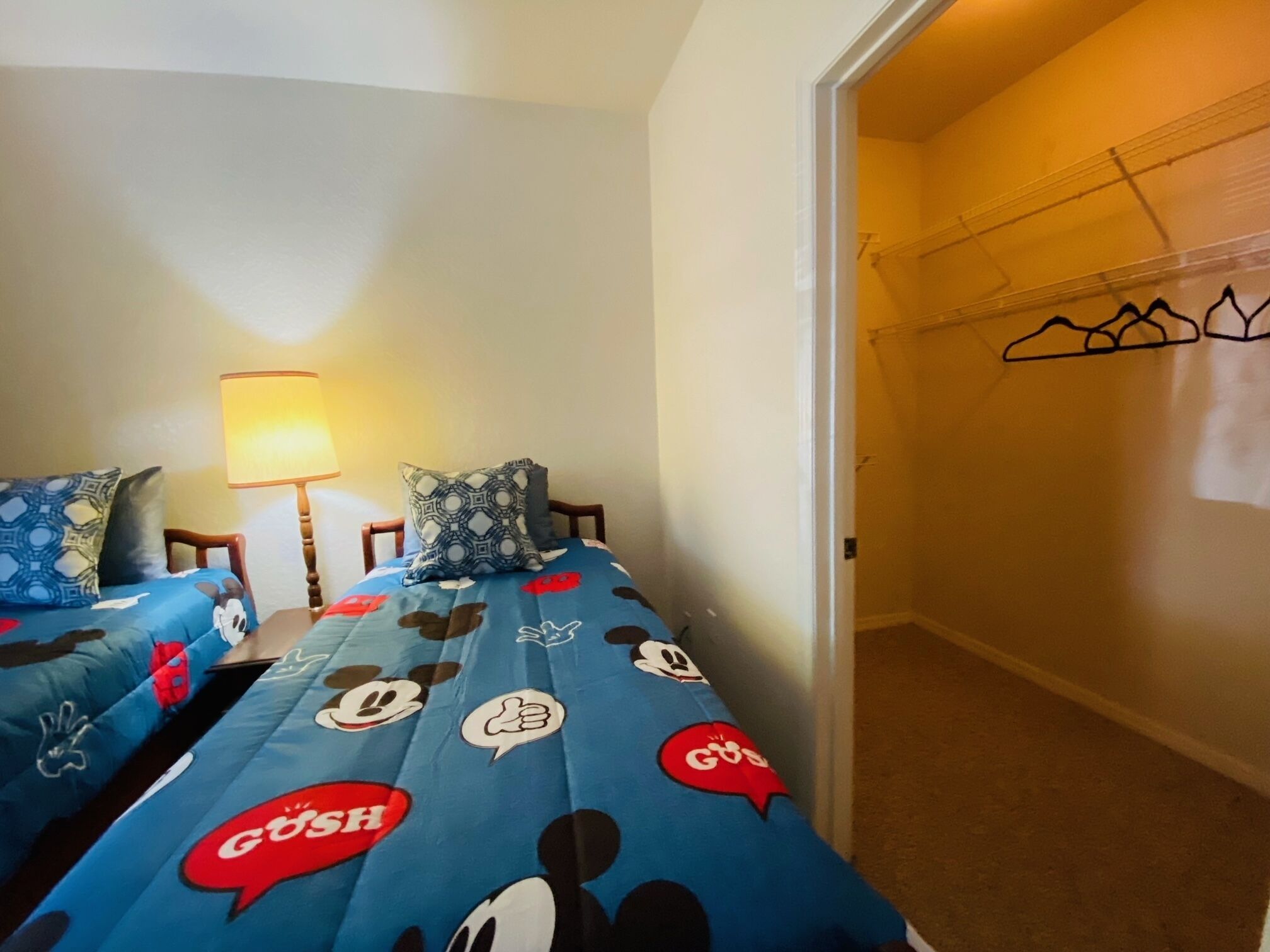 Une chambre avec deux lits, chacun agrémenté de draps et de couvertures aux motifs de Mickey Mouse. Une lampe se trouve sur un côté de la pièce.