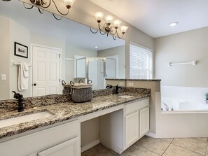 A bathroom with a large mirror, granite countertop, white cabinets, a bathtub, and a shower. - Anthony's Southern Dunes Vacation Home (Haines City)