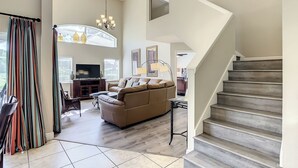 A spacious living room with a large sofa, a television, and a staircase leading to an upper floor.