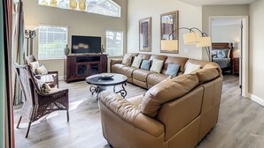 A spacious living room with a large sectional sofa, a television, and a dining area with a round table.