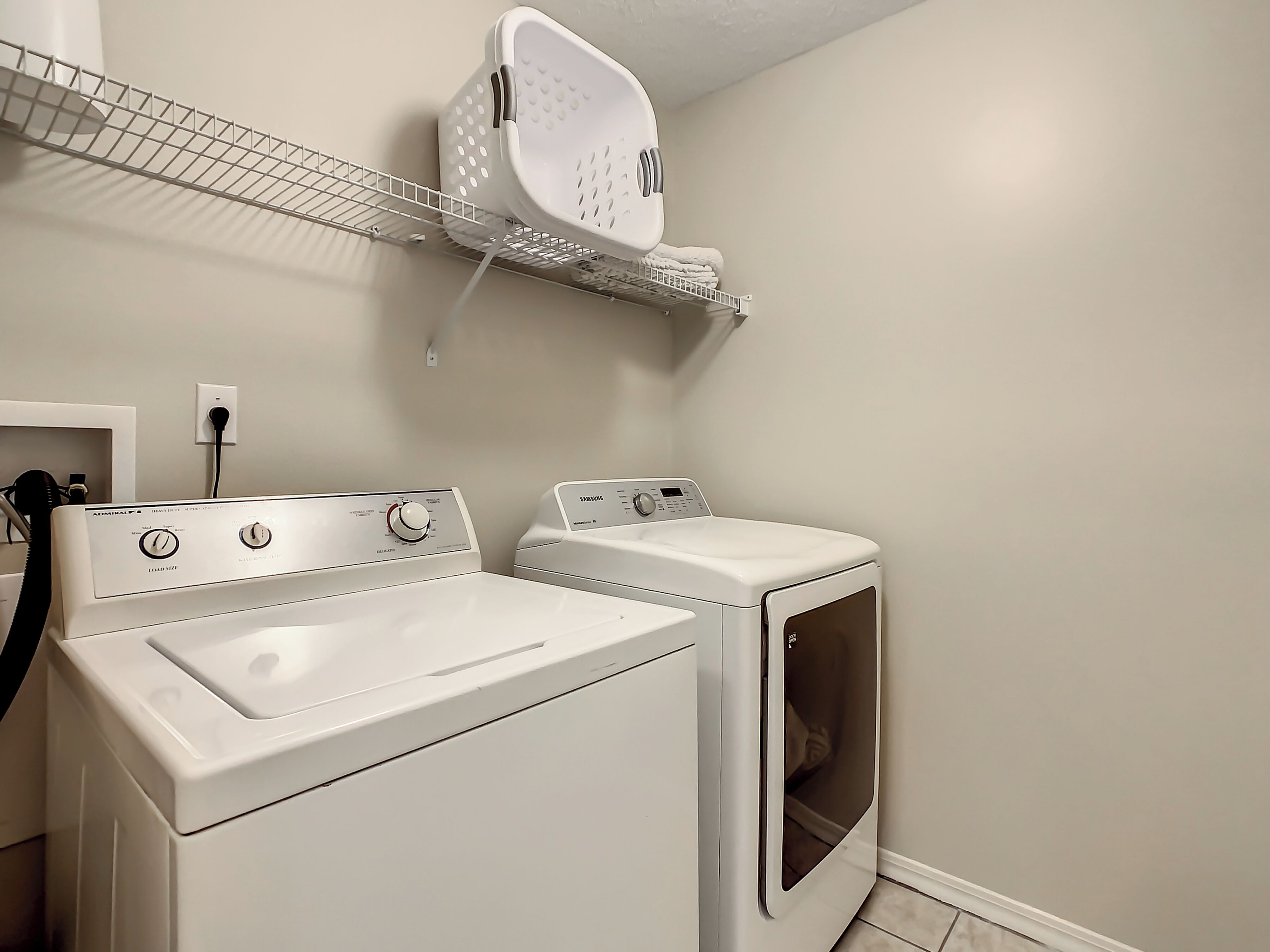 A laundry area with two white washing machines, a drying rack, and a wall-mounted basket.