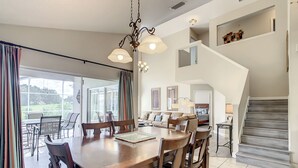 A spacious dining area with a wooden table and chairs, a chandelier, and a view through large glass doors to an outdoor patio.