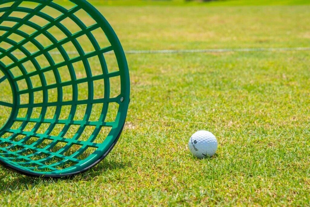 A golf ball on a grassy field with a green golf club head in the foreground.