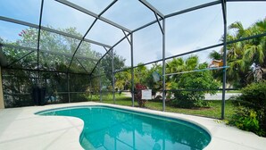 An indoor swimming pool with a curved edge, surrounded by a glass enclosure and lush greenery.