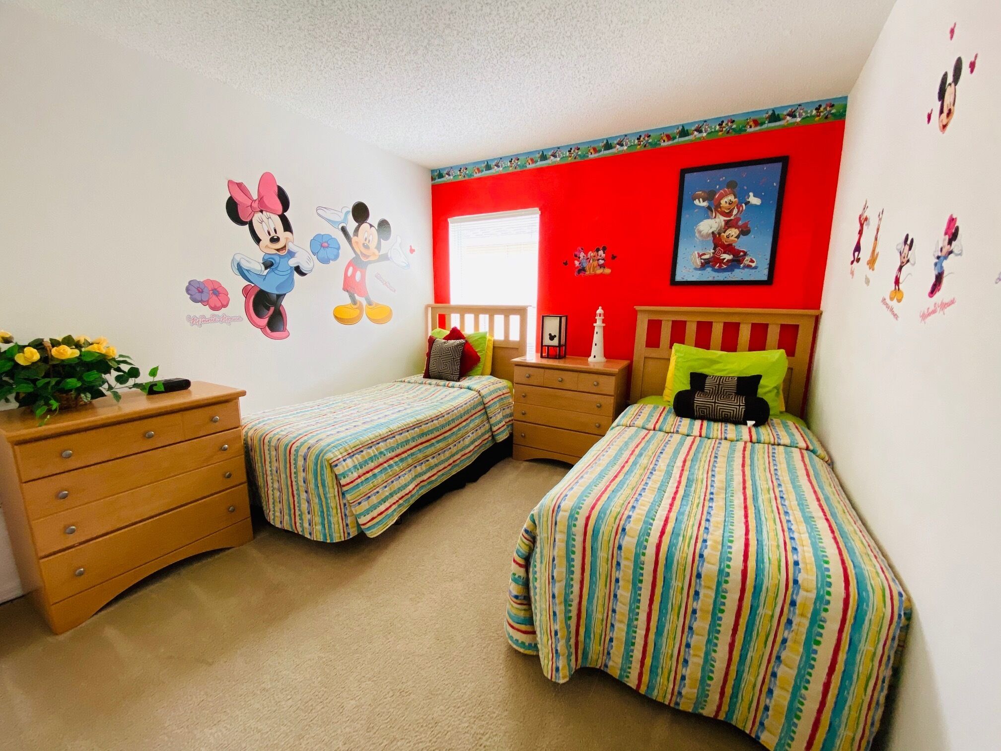 Habitación infantil con dos camas, un aparador y calcomanías de pared de Mickey Mouse.