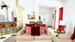 A living room with a beige sofa set, a green rug, and red cushions.