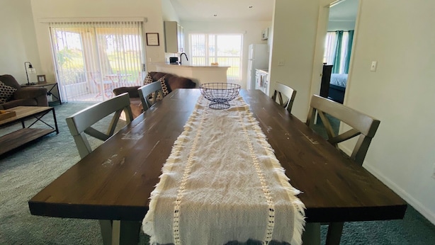 Uma ampla sala de jantar com uma longa mesa de madeira, cadeiras acolchoadas e um tapete tecido.