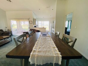 Un vaste espace dédié à la salle à manger, avec une longue table en bois, des chaises rembourrées et un chemin de table tissé.