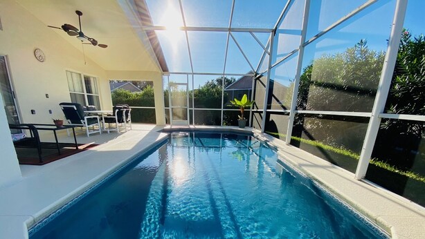 Une piscine à l’eau d’un bleu cristallin, entourée d’une structure en verre, et un espace patio aménagé avec du mobilier d’extérieur.