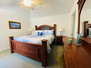 A bedroom with a wooden bed, two bedside tables with lamps, a dresser, a ceiling fan, and a framed picture on the wall.