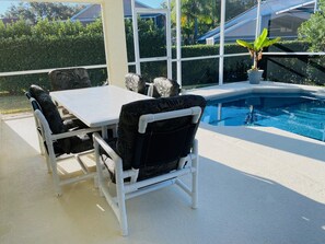 An outdoor patio with a pool, white furniture, and a potted plant.