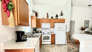 Cocina compacta con armarios de madera, un refrigerador blanco, estufa y cafetera.