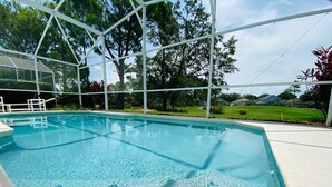 Una piscina cristalina con un borde de baldosas, rodeada por una estructura metálica blanca y árboles.