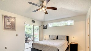 A bedroom with a bed, a ceiling fan, a window, and a door.