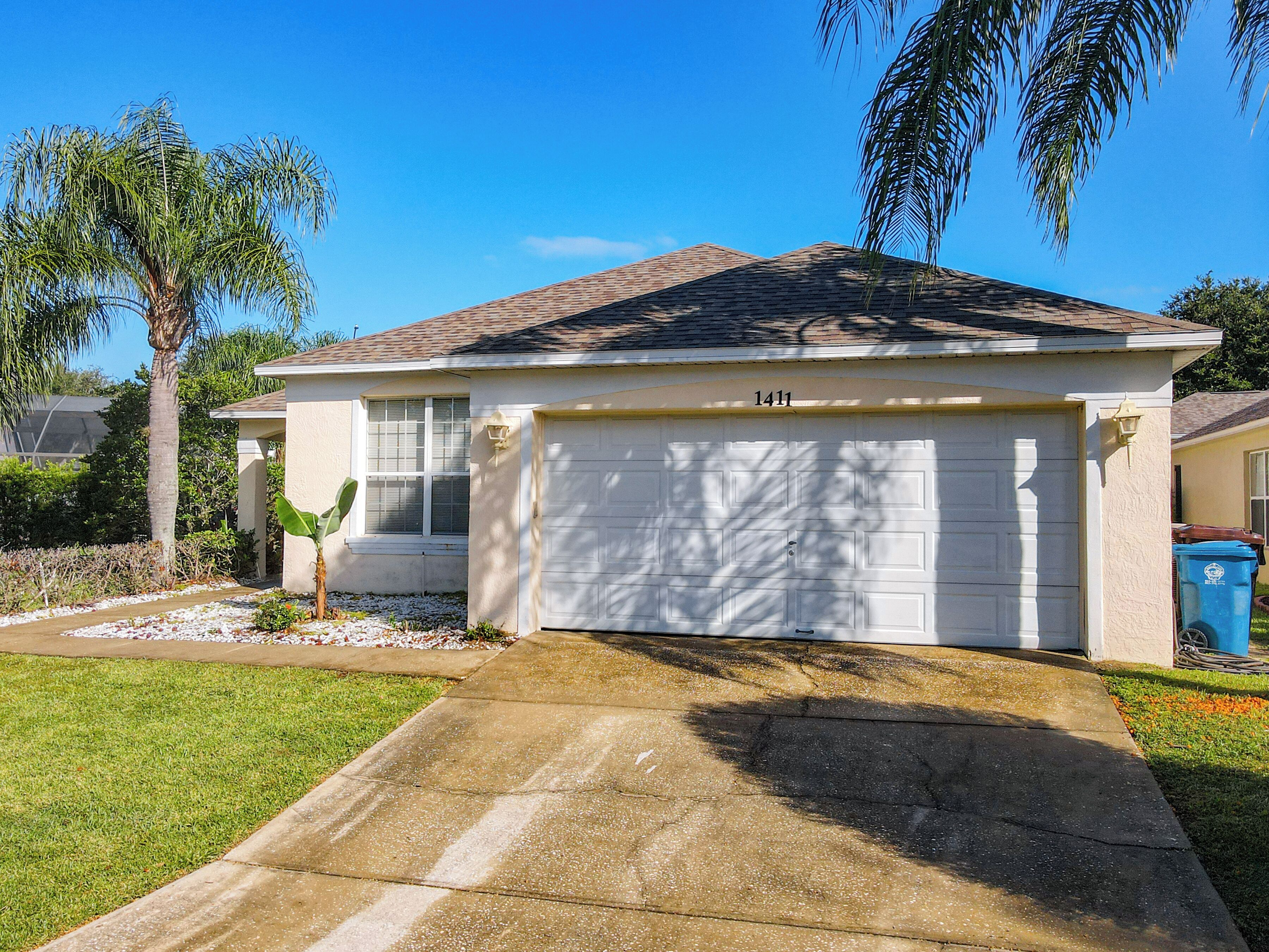 A single-story house with a garage, a well-maintained lawn, and a palm tree.