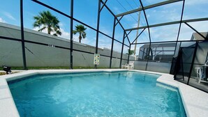 A swimming pool with clear blue water, surrounded by a metal fence and a white wall. - Mike's Southern Dunes Vacation Home (Haines City)