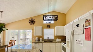 A kitchen with granite countertops, white cabinets, a refrigerator, and a coffee maker. - Mike's Southern Dunes Vacation Home (Haines City)