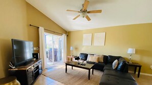 A living room with a flat-screen TV, a sofa, a coffee table, and a ceiling fan.