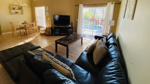 A living room with a black leather sofa, a television, and a dining area with a table and chairs.