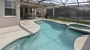 Une piscine au design incurvé, entourée d’un patio abrité comprenant des chaises et une table.