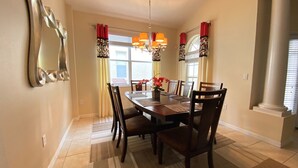 Une salle à manger avec une table ronde, six chaises, un lustre et un grand miroir au mur.