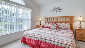 A bedroom with a large window, a wooden headboard, two bedside tables with lamps, and a decorative wall piece. - Maria's Southern Dunes Vacation Home (Haines City)