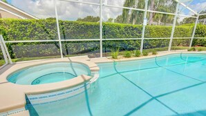 A swimming pool with a hot tub, surrounded by a glass enclosure and a hedge. - Maria's Southern Dunes Vacation Home (Haines City)