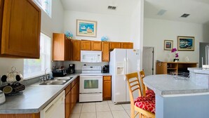 A kitchen with wooden cabinets, a microwave, a stove, and a refrigerator. There is a dining area with a table and chairs. - Dennis' Southern Dunes Vacation Home (Haines City)