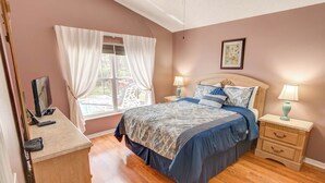 A bedroom with a bed, two bedside tables, a desk, and a window with curtains.