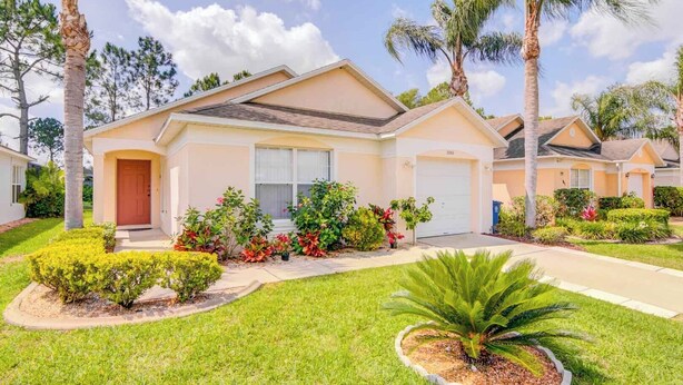 A single-story house with a front porch, a garage, and a well-maintained lawn with various shrubs and a palm tree.