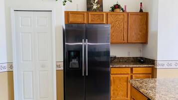 Una cocina con refrigerador de acero inoxidable, armarios de madera, encimera de granito y una puerta con un letrero que dice 'Live Love'.