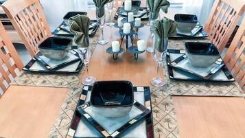 Una mesa de comedor dispuesta con platos cuadrados, vasos y servilletas.