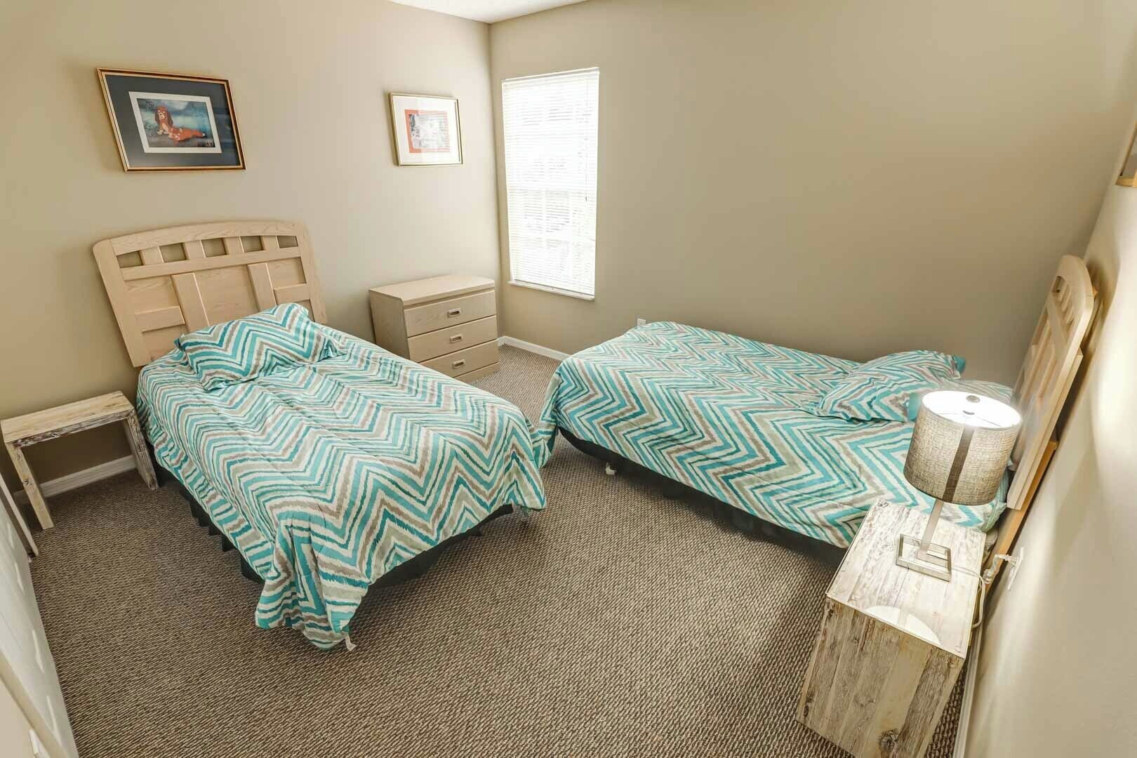 A bedroom with two beds, a small dresser, a nightstand, a lamp, and two framed pictures on the wall.