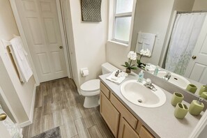 Une salle de bain avec des toilettes, un lavabo et un miroir. Des serviettes sont accrochées au mur et une petite plante est posée sur le comptoir.