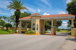 A gated entrance with a covered canopy, palm trees, and a clear sky.