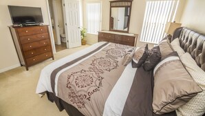 A bedroom with a large bed, a dresser, a TV, a mirror, and a door leading to another room. - Lake View Townhome Near Disney (Kissimmee)