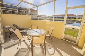 A covered patio with a round table and four chairs, overlooking a body of water and buildings.