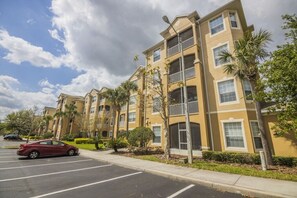 A multi-story residential building with balconies, a parking lot, and palm trees. - Amazing Condo in Windsor Hills - Close to Disney (Kissimmee)