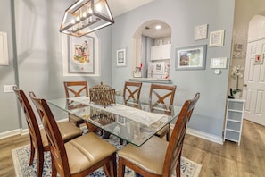 A dining room with a glass table, wooden chairs, a chandelier, and framed pictures on the walls. - Amazing Condo in Windsor Hills - Close to Disney (Kissimmee)